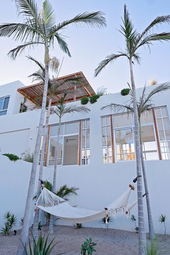 A modern building with large windows, a hammock, and palm trees. - Piscina Suite Sur At Topia (El Pescadero)
