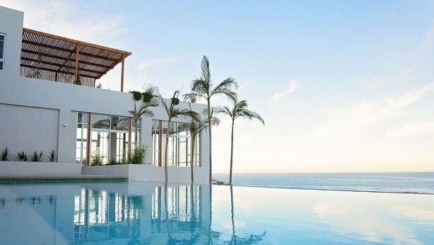 Ein modernes Gebäude mit Pool und Palmen, mit Blick auf den Ozean.