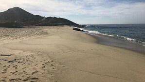 Ein weiter Sandstrand mit Fußabdrücken, eine felsige Küstenlinie und ein Berg im Hintergrund.