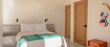 A bedroom with a bed, a nightstand, a wooden bench, and a wall-mounted decoration.