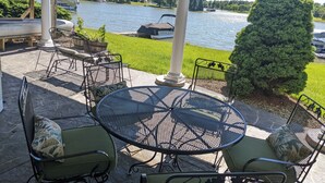 Un patio exterior con una mesa redonda y sillas, una parrilla y vistas a un lago con barcos.