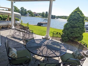Patio esterno con tavolo rotondo e sedie, un barbecue e vista su un lago con barche.