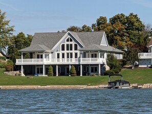 A large, two-story house with a wrap-around porch, a garage, and a dock extending into a body of water.