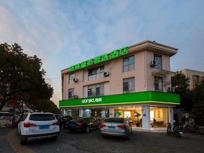 A hotel with a green and white facade, multiple floors, and a parking area with several cars.