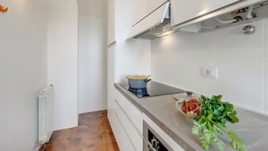 A modern kitchen with white cabinets, a built-in stove, and a countertop with fresh vegetables. - Villa Fiorita (Sirmione)