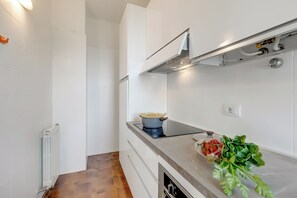 Une cuisine moderne avec des meubles blancs, une cuisinière encastrée et un plan de travail où sont disposés des légumes frais.