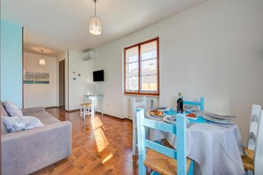 A dining area with a table set for two, a sofa, and a television on the wall.