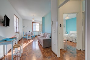 A room with a sofa, a dining table, a TV, and a bed. - Villa Fiorita (Sirmione)