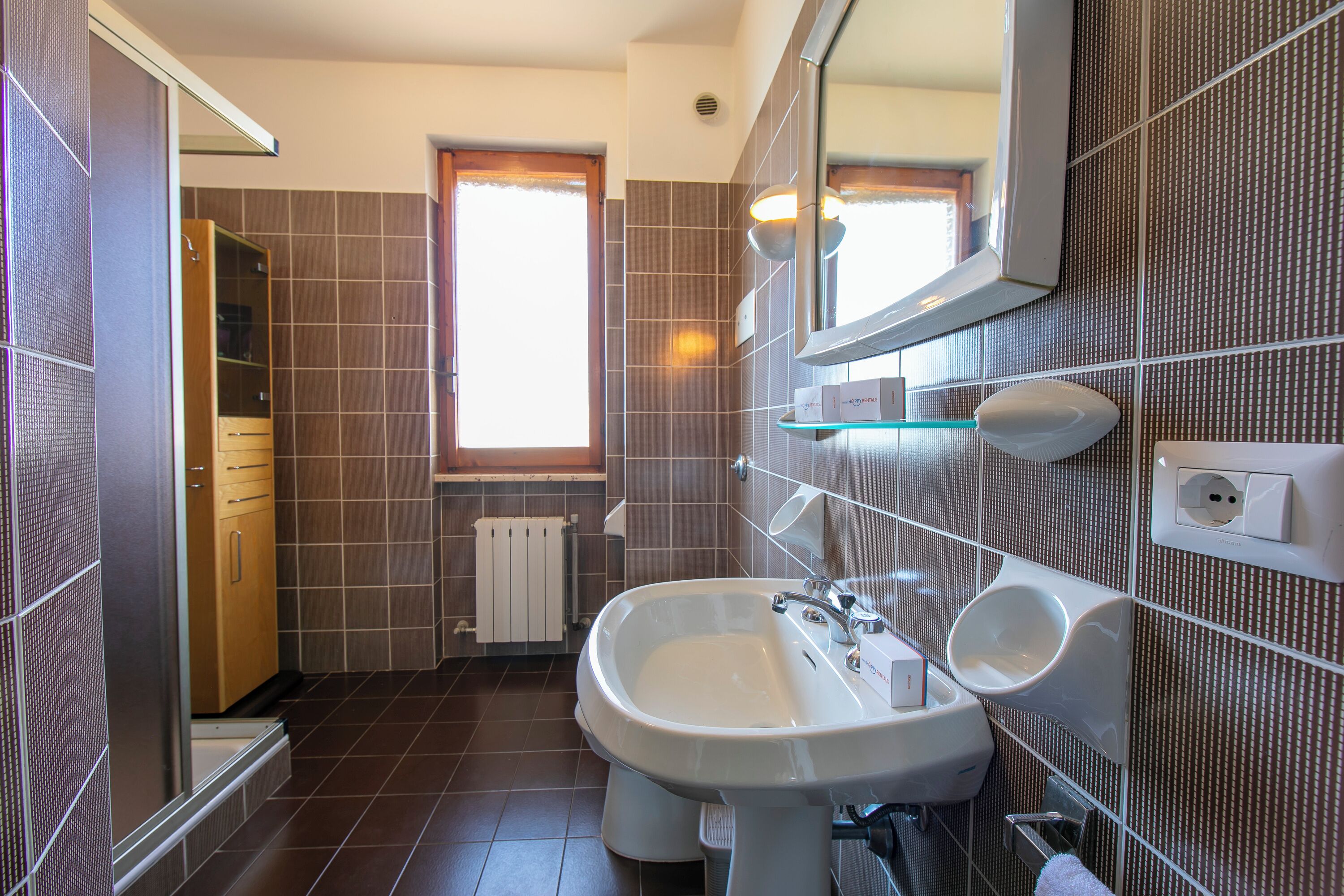 A modern bathroom with a large sink, mirror, and a window providing natural light.
