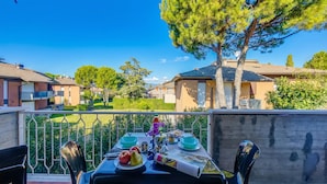 A balcony with a table set for dining, overlooking a residential area with houses and trees. - Villa Fiorita (Sirmione)