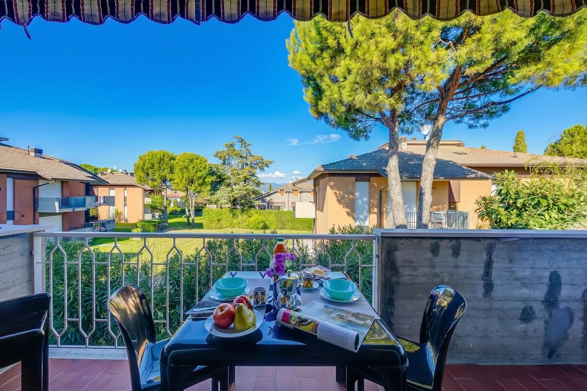 A balcony with a table set for dining, overlooking a residential area with houses and trees.