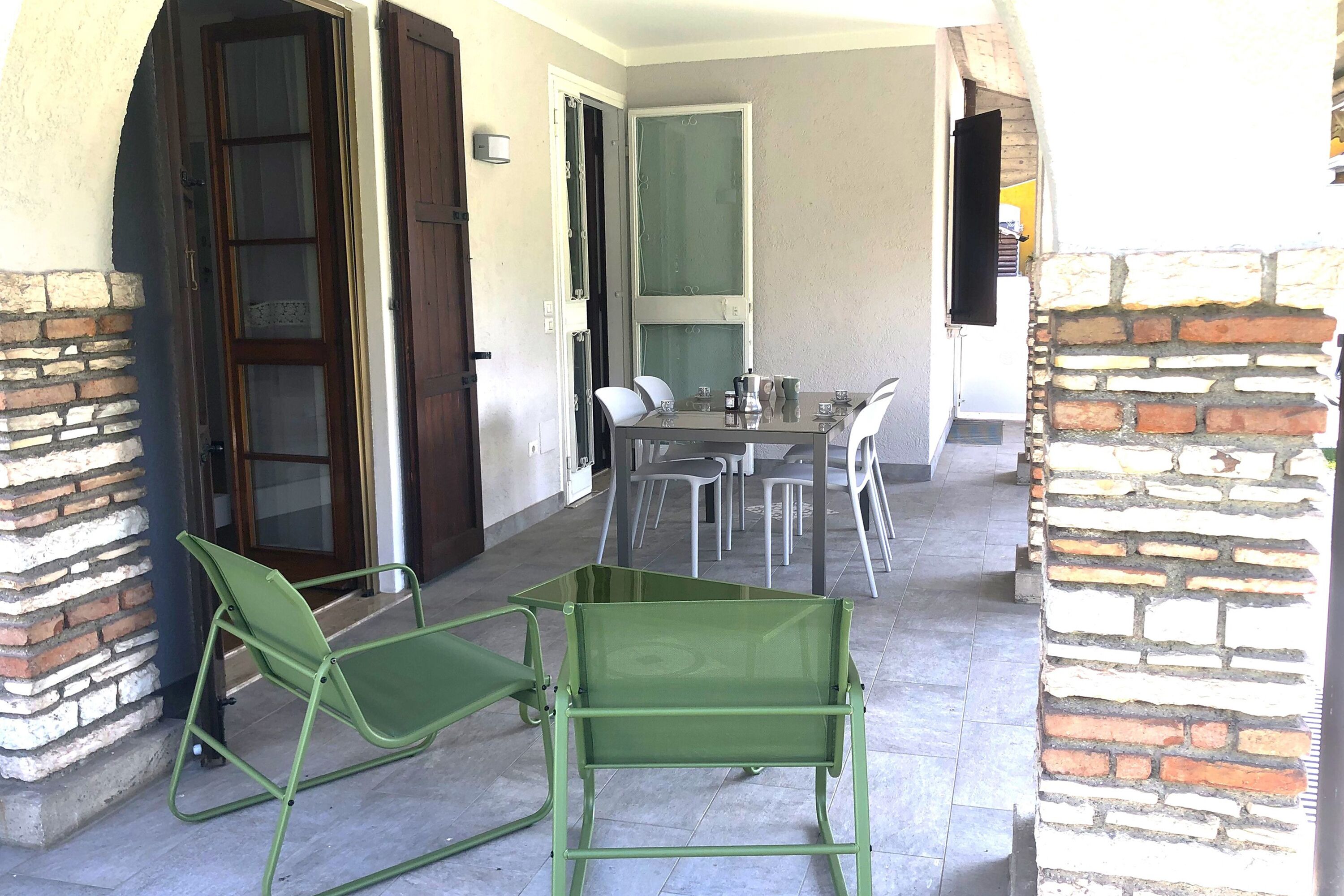Uma área de pátio com uma mesa, cadeiras, uma cadeira verde e uma parede de tijolos.
