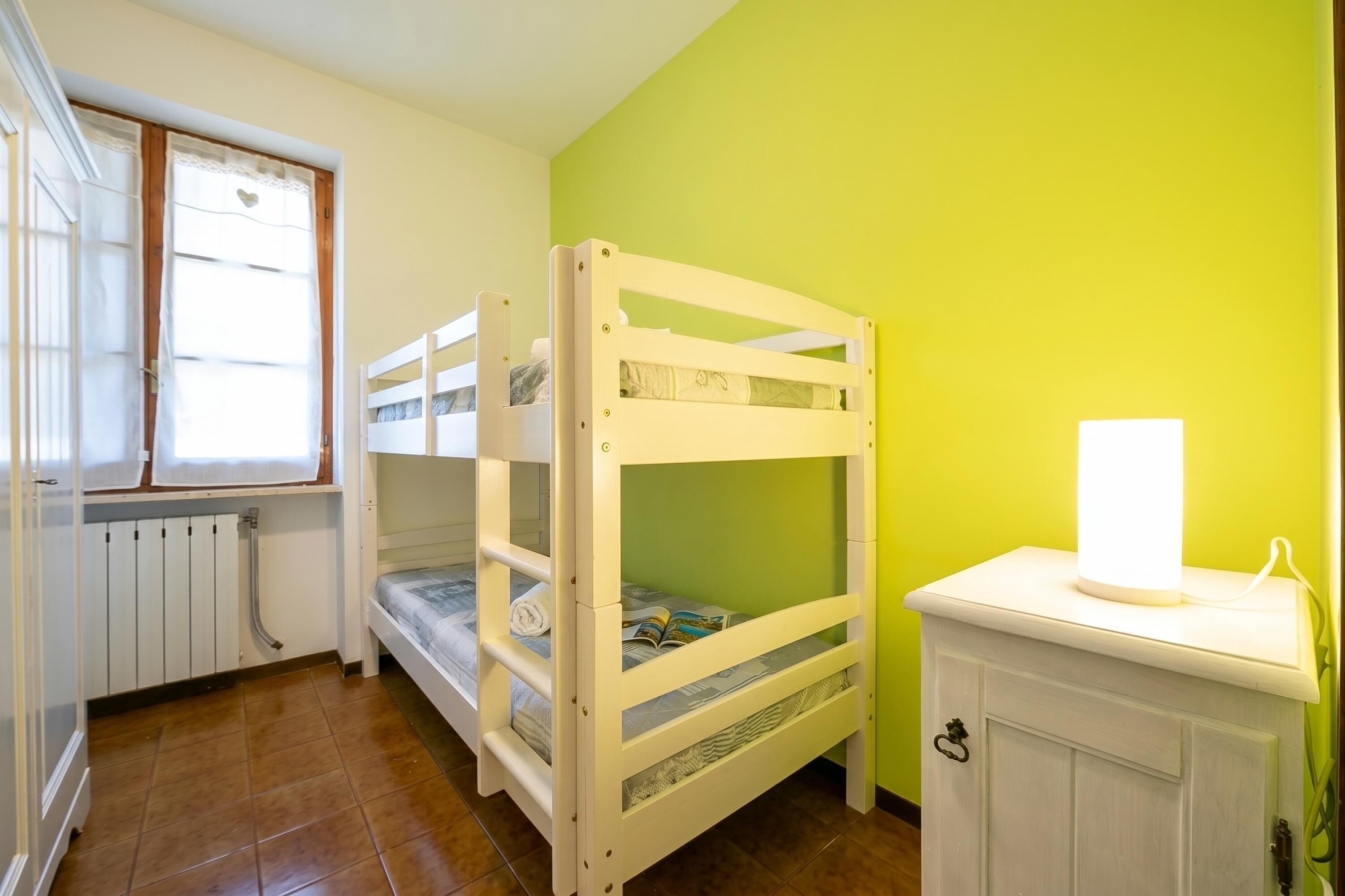 A bunk bed room with a window, radiator, and a bedside table with a lamp.