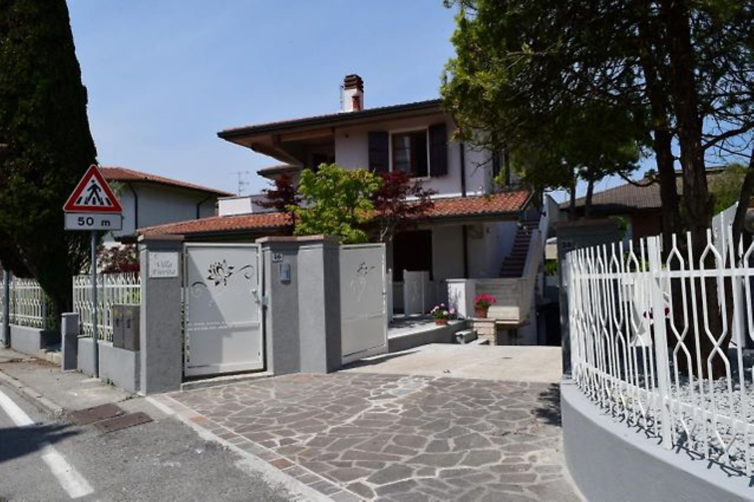 Una entrada protegida por una reja a una propiedad residencial, con un camino de piedra que conduce a una casa con techo de tejas.