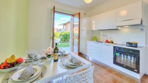 A modern kitchen with white cabinets, a built-in oven, and a dining area with a table set for two. - Villa Fiorita (Sirmione)