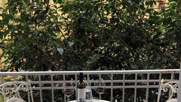 A balcony with a round table set for dining, surrounded by white metal chairs with fish designs.