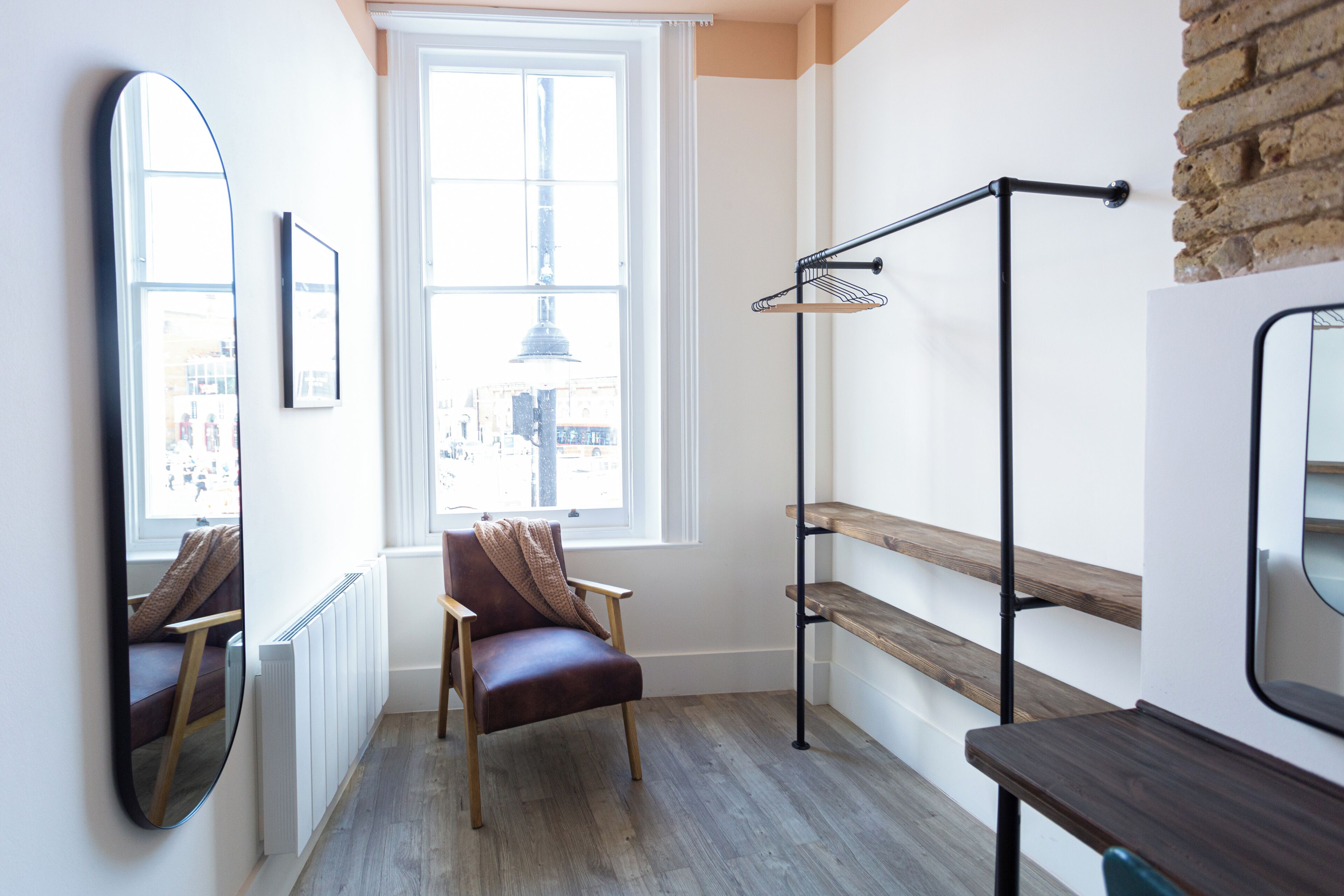 A room with a large window, a chair, a floor lamp, and a mirror.