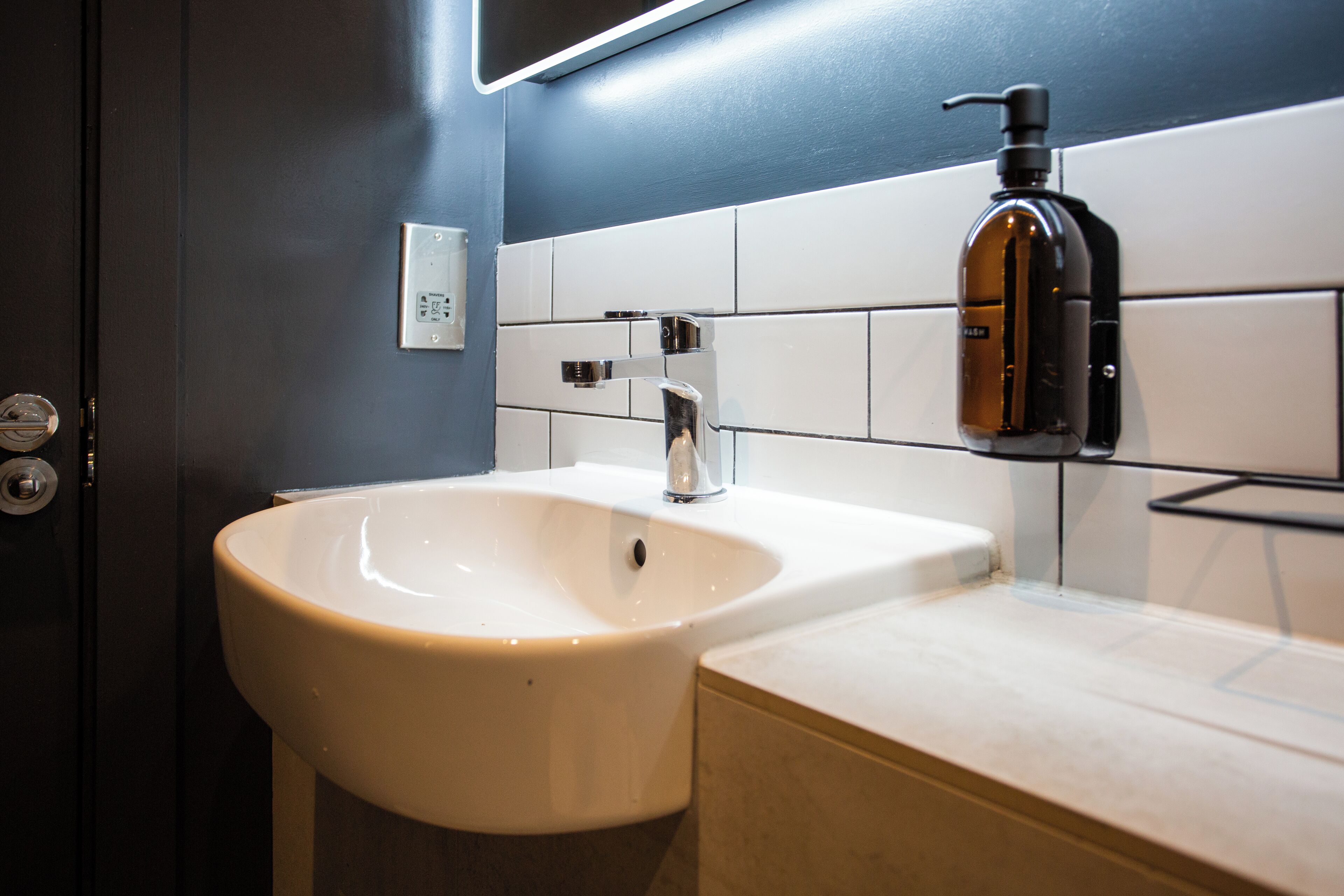 Een badkamer met een wit wastafel, een zwarte zeepdispenser en een wandlamp.