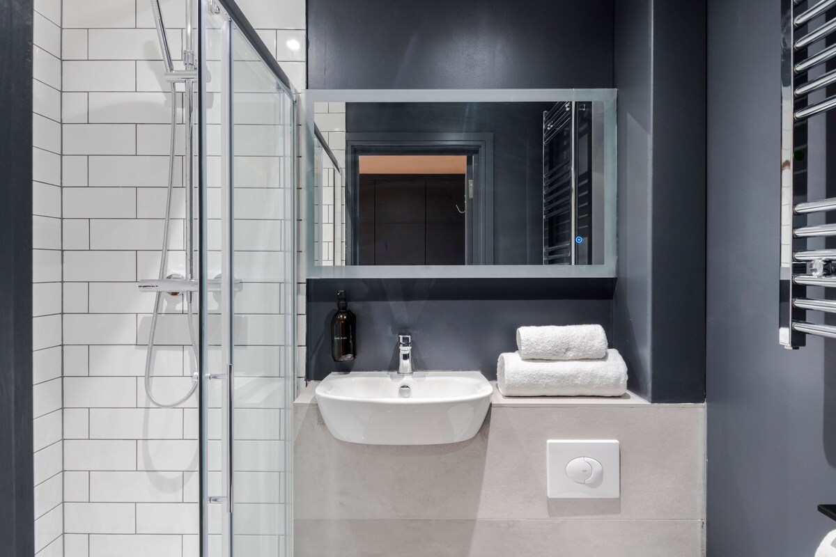 A modern bathroom with a glass shower enclosure, a white sink, and a mirror above it.