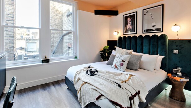 Un dormitorio con un ventanal grande, una cama con cabecera oscura y dos lámparas fijadas a la pared.