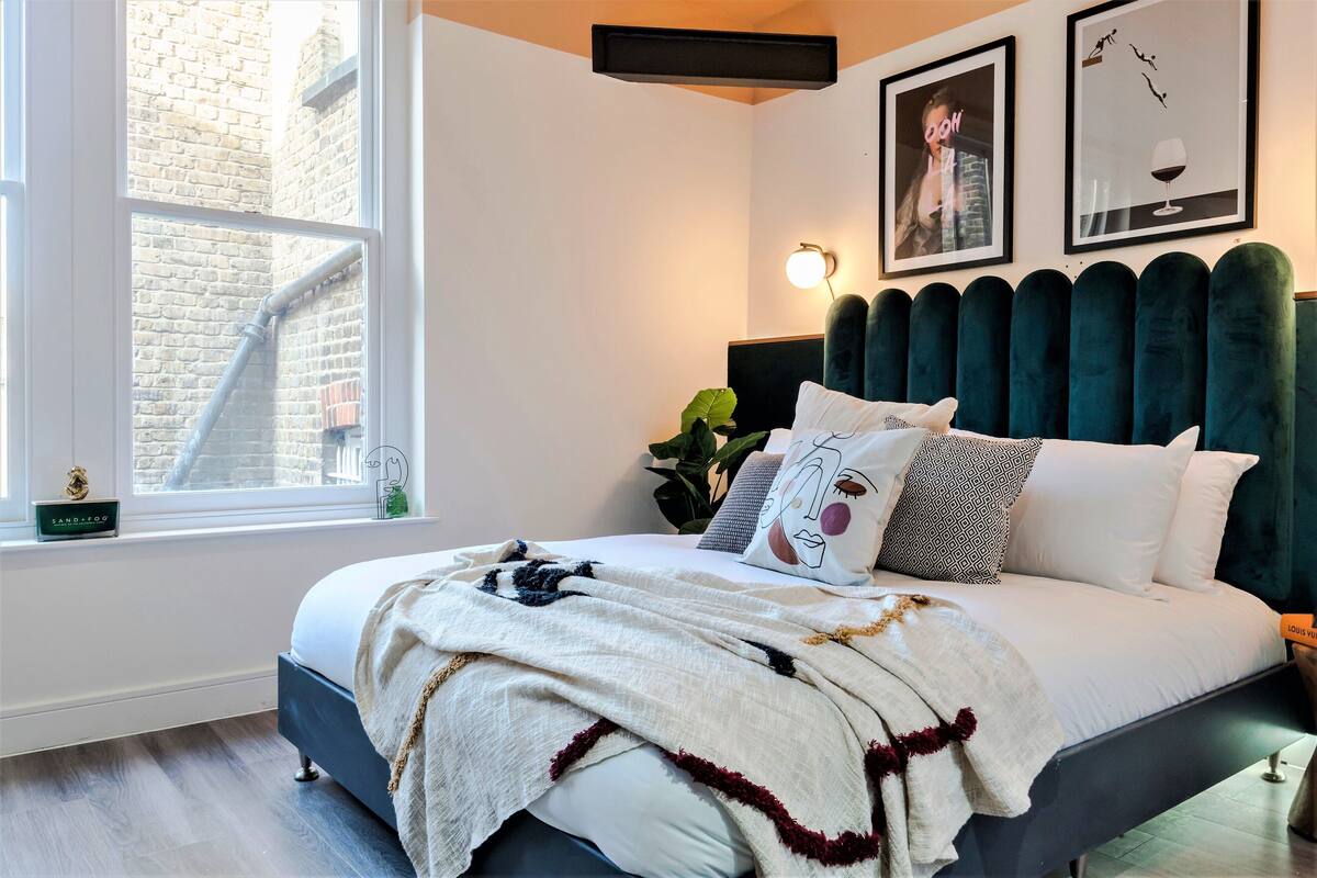 A bedroom with a bed, a window, a plant, and artwork on the wall.