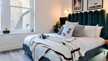 A bedroom with a bed, a window, a plant, and artwork on the wall.
