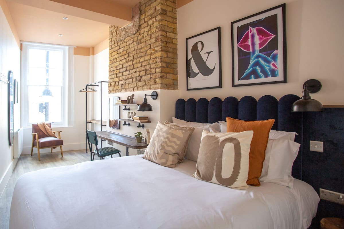 A bedroom with a large bed, a desk, and a chair. There is a brick wall and a window.