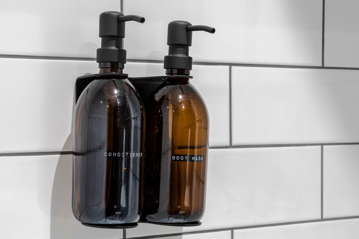 Two bottles of body wash and conditioner on a tiled wall.