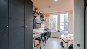 Una cocina moderna con armarios oscuros, una zona de comedor con dos sillas y una ventana con vistas a edificios.