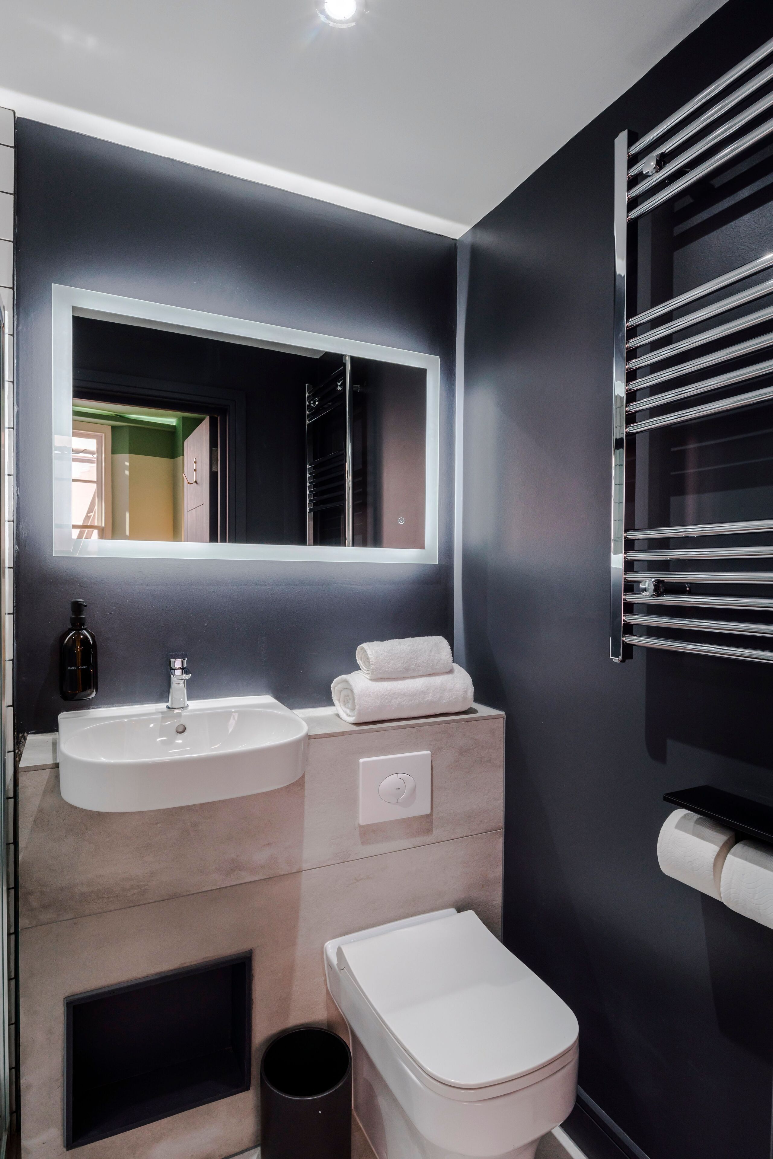 Ein modernes Badezimmer mit einem großen Spiegel, zwei Waschbecken, einer Toilette und einem Handtuchhalter.