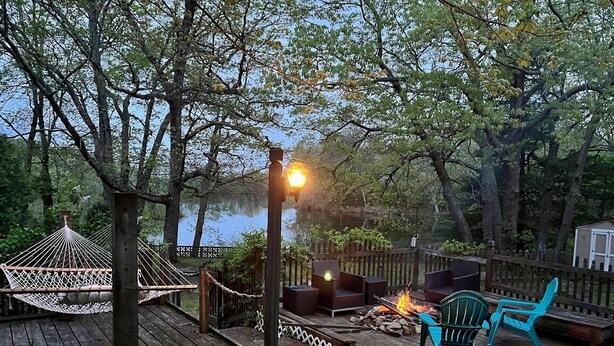Une terrasse en bois avec un hamac, des sièges d’extérieur et un foyer.