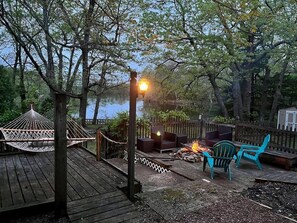 A wooden deck with a hammock, outdoor seating, and a fire pit.
