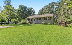 A single-story house with a front porch, surrounded by a well-maintained lawn and trees.