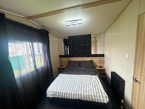 Een slaapkamer met een bed, nachtkastje, lamp, raam met gordijnen en een muur met een geometrisch patroon.
