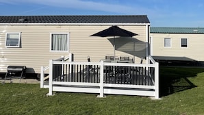 A mobile home with a fenced patio area, a grill, and a clear blue sky. - Fluffy Caravan Sleeps 4, Pet-friendly (Sheerness)