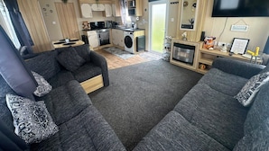 A compact RV interior with a kitchenette, two sofas, a flat-screen TV, and a fireplace. - Fluffy Caravan Sleeps 4, Pet-friendly (Sheerness)
