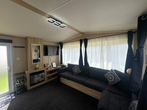 A compact living space with a sofa, television, and a small entertainment unit. - Fluffy Caravan Sleeps 4, Pet-friendly (Sheerness)
