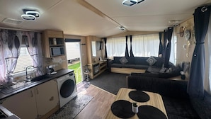 A compact RV interior with a kitchenette, a sofa, and a dining area. - Fluffy Caravan Sleeps 4, Pet-friendly (Sheerness)