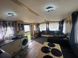 A compact RV interior with a kitchenette, a sofa, and a dining area. - Fluffy Caravan Sleeps 4, Pet-friendly (Sheerness)