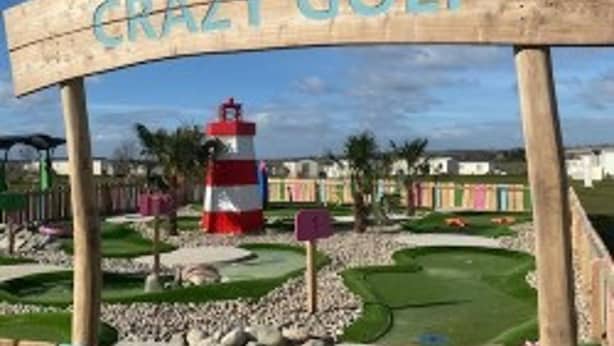 A wooden sign with the text "CRAZY GOLF" and a miniature golf course with a red and white lighthouse in the background. - Fluffy Caravan Sleeps 4, Pet-friendly (Sheerness)