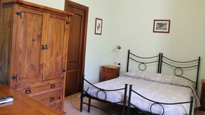 A bedroom with a wooden wardrobe, a metal bed frame, a bedside table, and two framed pictures on the wall. - Amalfi double room (Gragnano)