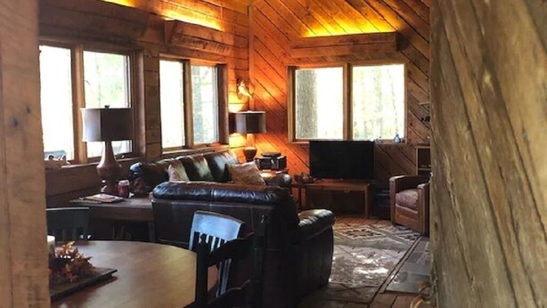 Interior acogedor de una cabaña con techo de madera, un sofá, televisor y comedor.