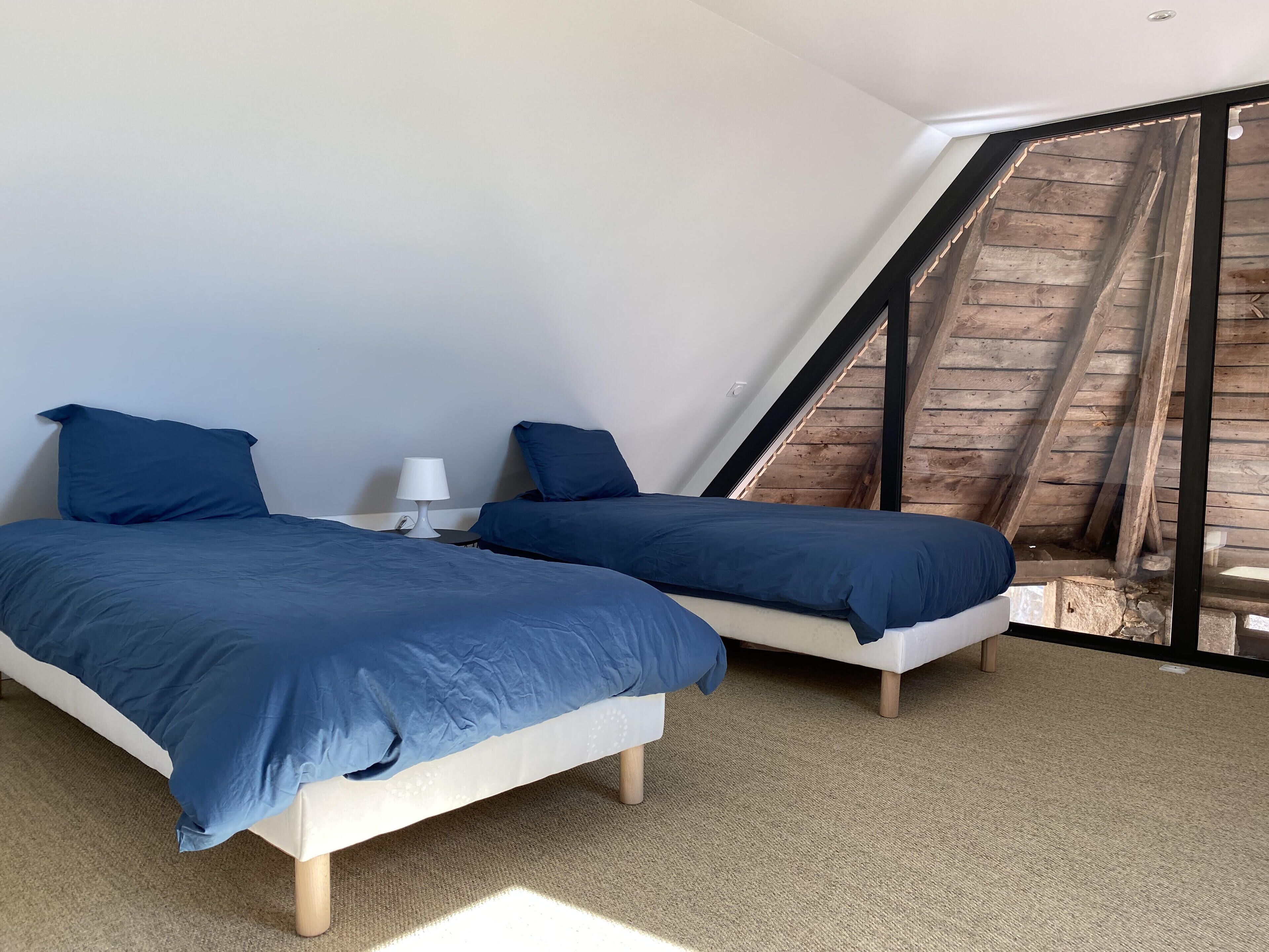 Ein Schlafzimmer mit zwei Betten, einer weißen Lampe und einer schrägen Decke mit freiliegenden Holzbalken.