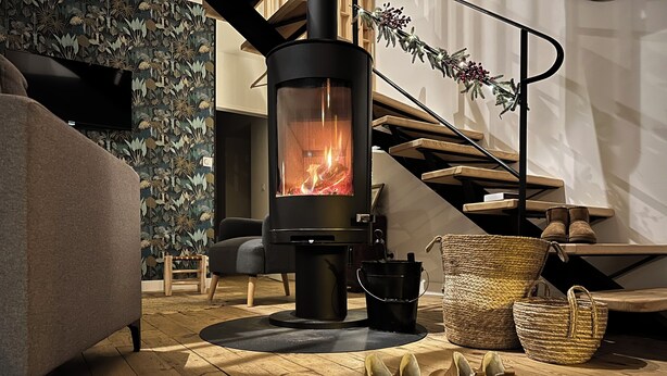 Ein gemütliches Wohnzimmer mit Kaminofen, bequemer Couch, Treppe und dekorativem Girlande.