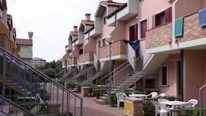 A residential building with multiple balconies, a central staircase, and outdoor seating areas.