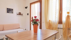 A wooden dining table with a potted plant, white chairs, a sofa, and a window with curtains.