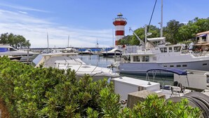 Un puerto deportivo con barcos amarrados, un faro al fondo y abundante vegetación en primer plano.