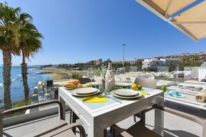 Une table dressée pour le dîner, avec vue sur la mer et des bâtiments en arrière-plan.