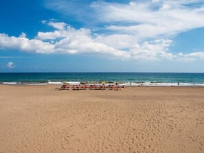 Une plage bordée de rangées de chaises longues et de parasols, un ciel dégagé et l’océan en toile de fond.