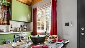 Un comedor con una mesa de madera dispuesta para dos personas, una olla grande sobre la mesa y una ventana con cortinas rojas.